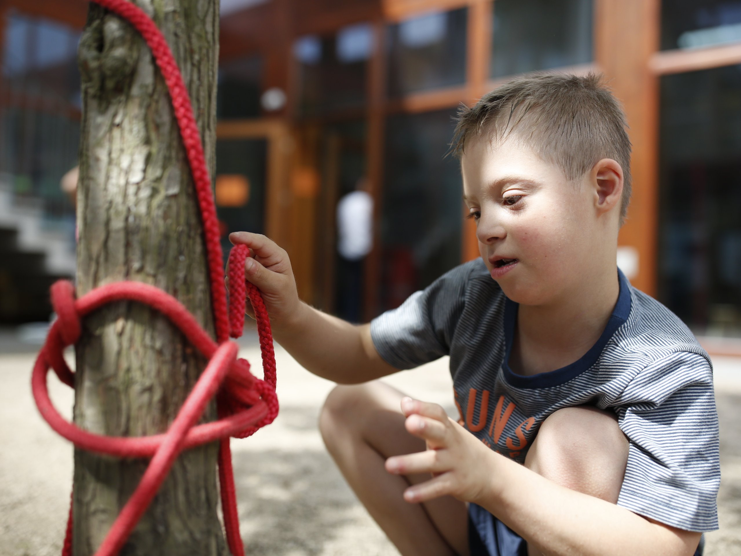 Foto von einem Jungen mit Down-Syndrom. Er spielt auf einem Spielplatz mit einem Seil.