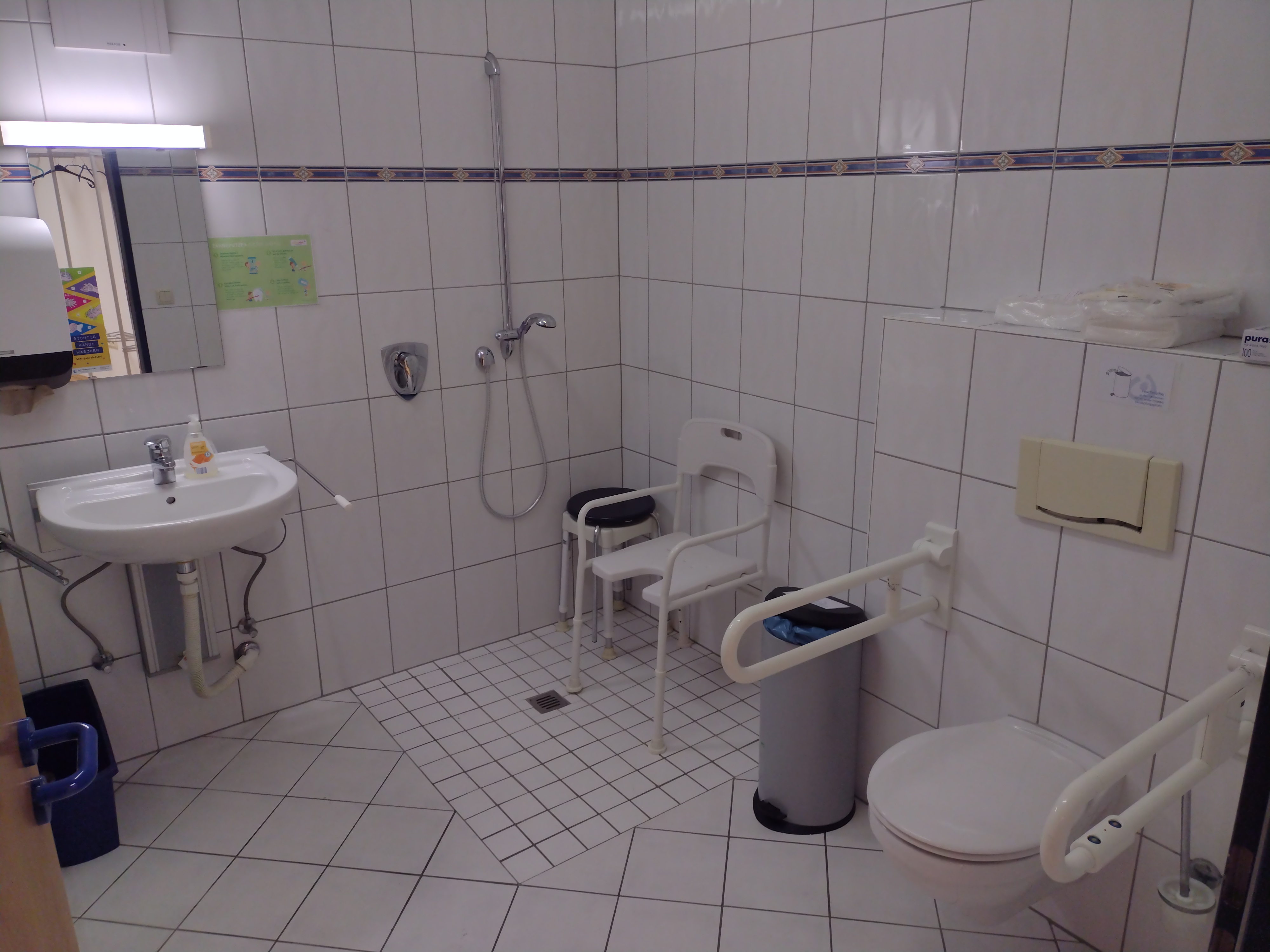 Foto vom barrierefreien Bad mit WC mit Haltegriffen, bodengleiche Dusche mit Dusch-Stuhl, höhenverstellbares Waschbecken, Waschmaschine.