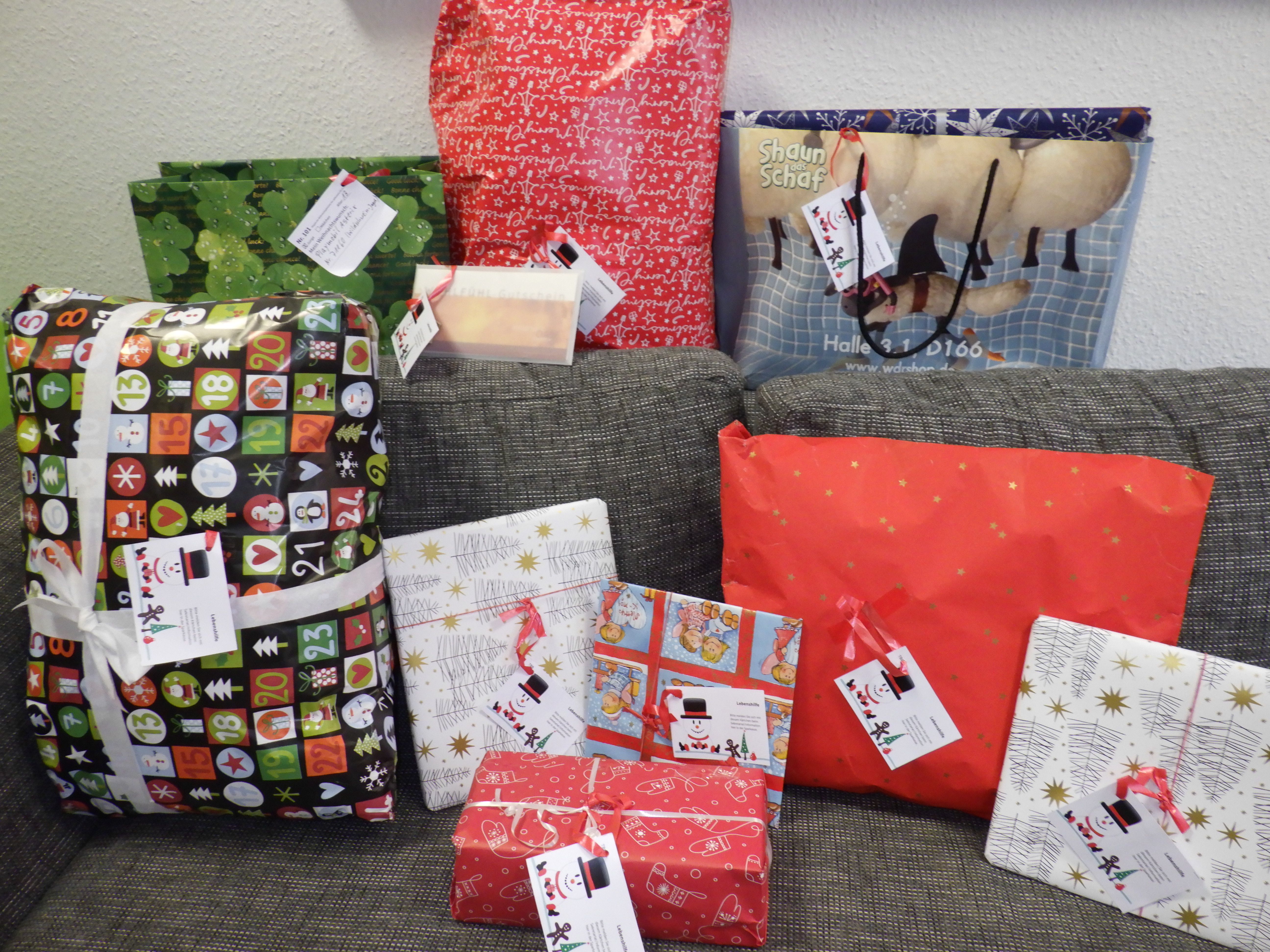 Ein Foto. Es sind 10 unterschiedlich verpackte Geschenke mit kleinen Anhängekärtchen auf dem Foto zu sehen. Manche sind mit Geschenkpapier verpackt, manche in Geschenktaschen.
