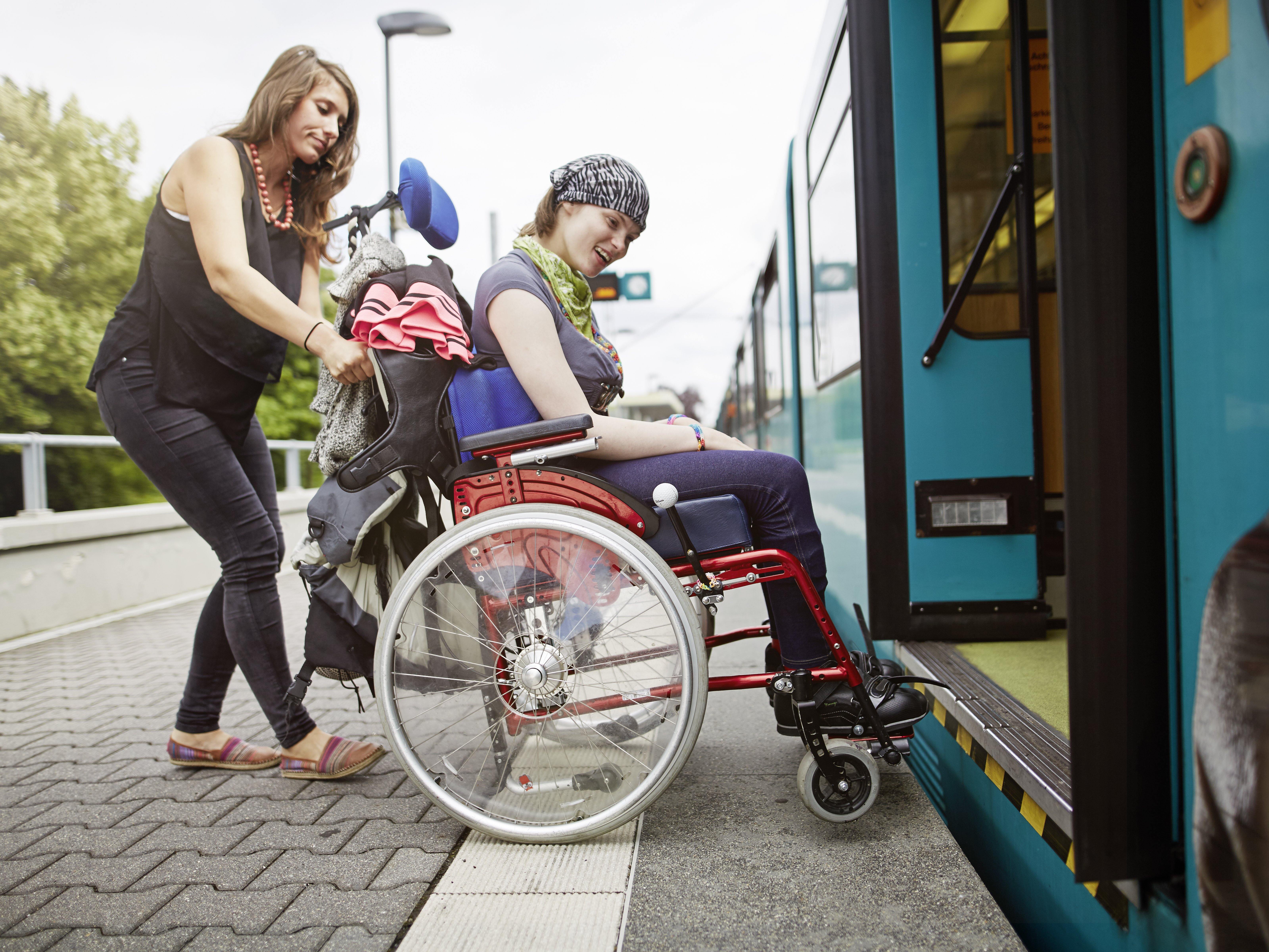 Foto: Eine Betreuerin schiebt eine Frau im Rollstuhl in einen Regionalzug.