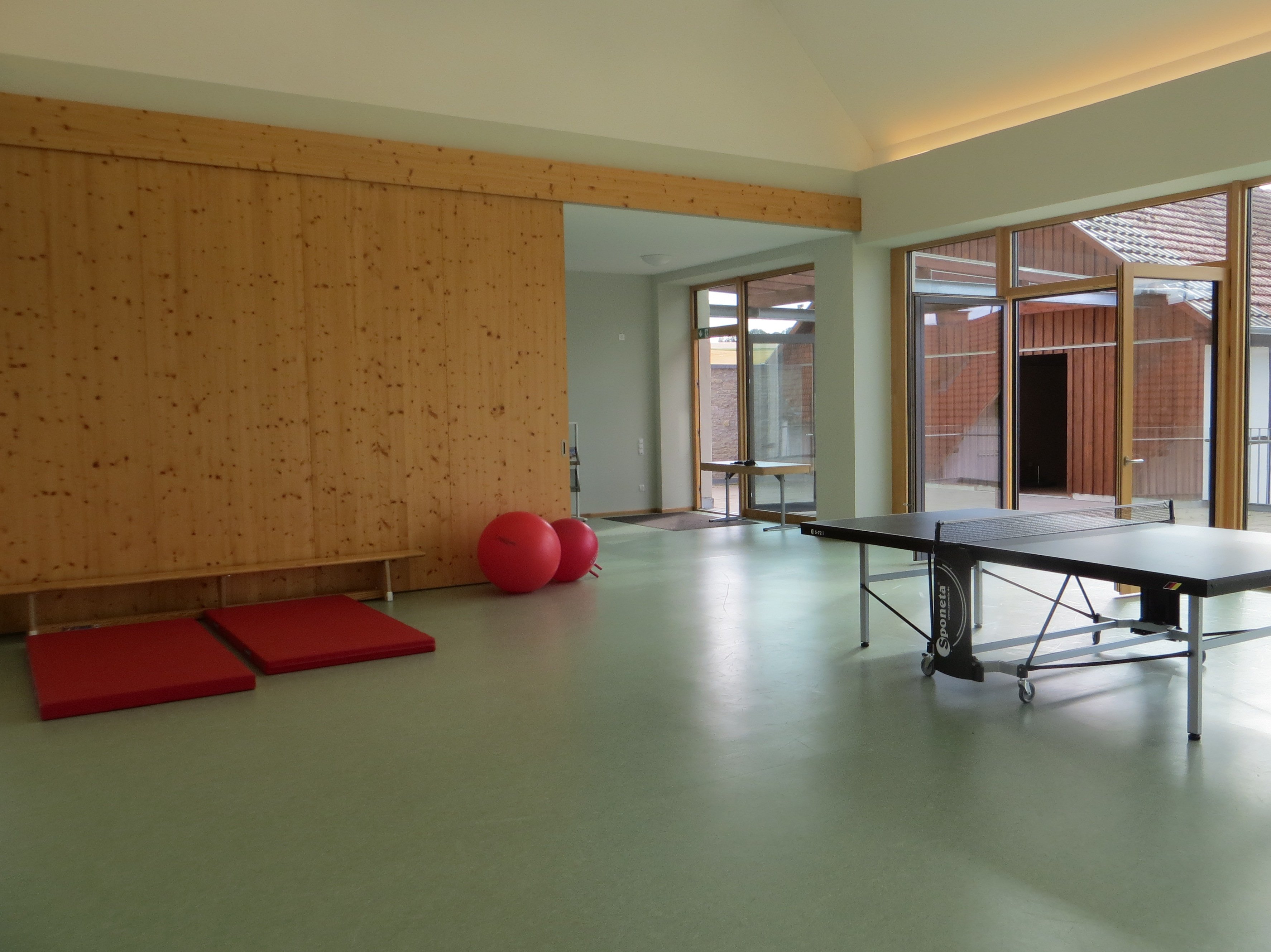 Foto der modernen Sporthalle mit Tischtennisplatte, Matten und Gymnastikbällen.