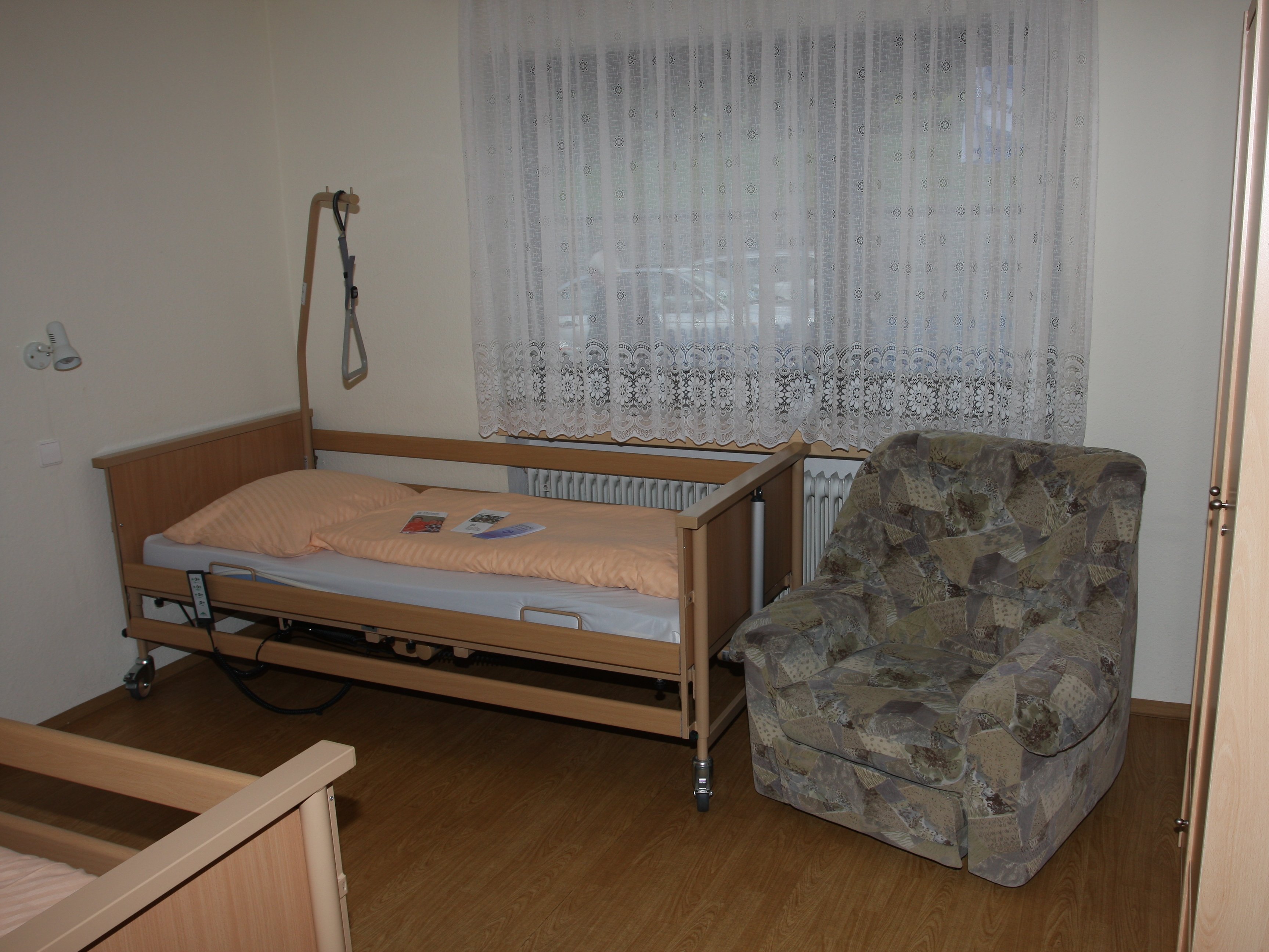 Foto eines Zimmers mit zwei Pflegebetten und einem gemütlichen Sessel.