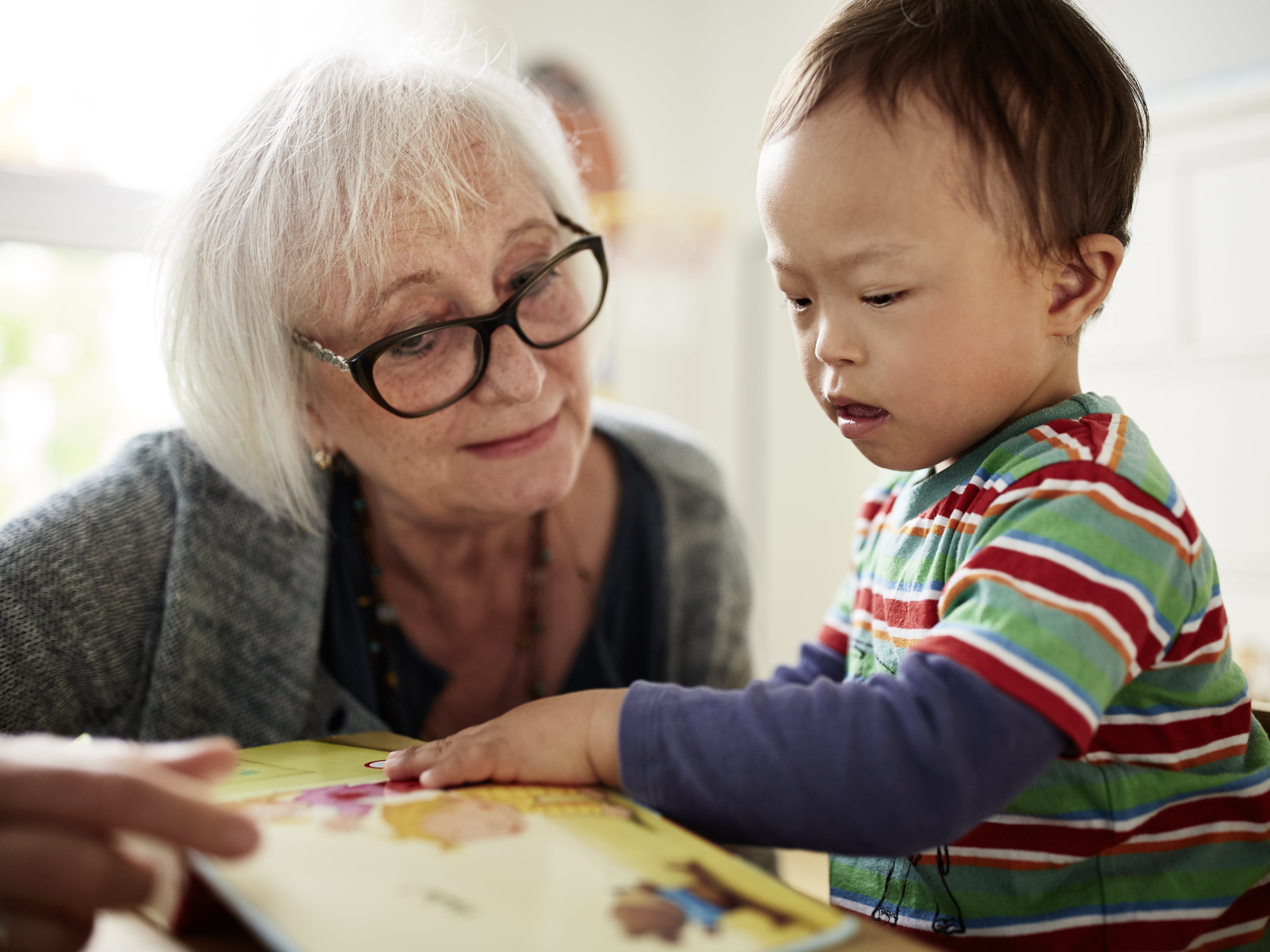 Foto von einem Jungen zwei Jahre alten Jungen. Er betrachtet zusammen mit einer Betreuerin der Lebenshilfe ein Bilderbuch.